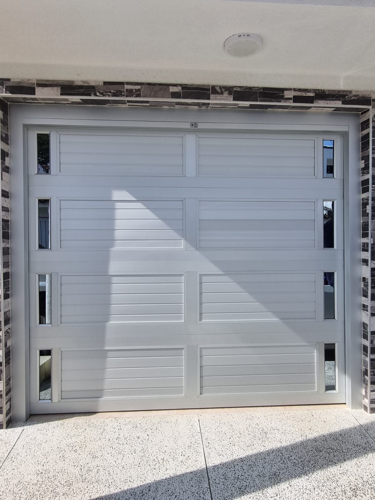 Una mampara de ducha de cristal de estilo neoangular con marco plateado, instalada en la esquina de un baño blanco, luminoso y moderno.