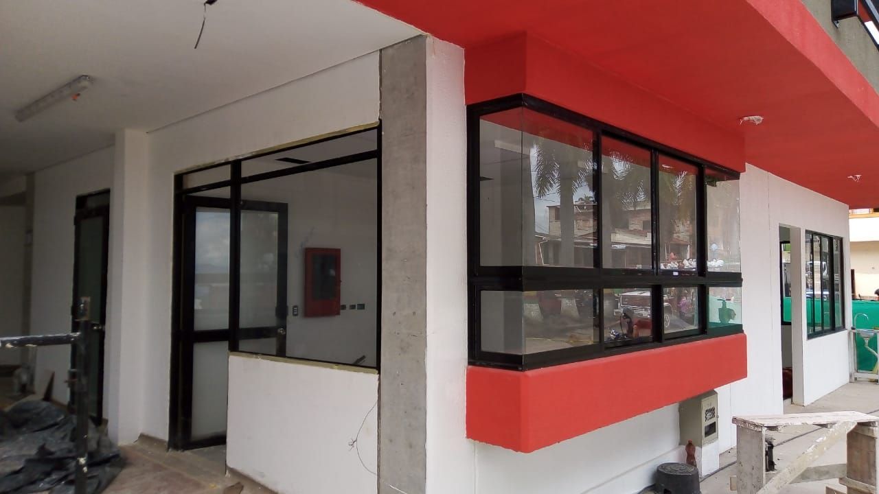 Primer plano de un marco de ventana blanco con mecanismo de cierre, con vistas a una obra en construcción borrosa.