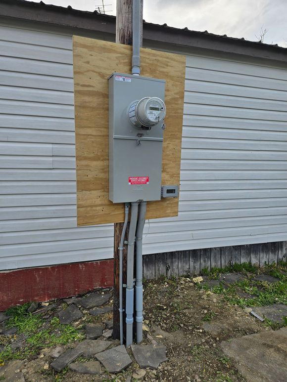 Outdoor air conditioner unit mounted on beige vinyl siding beside electrical boxes and conduit