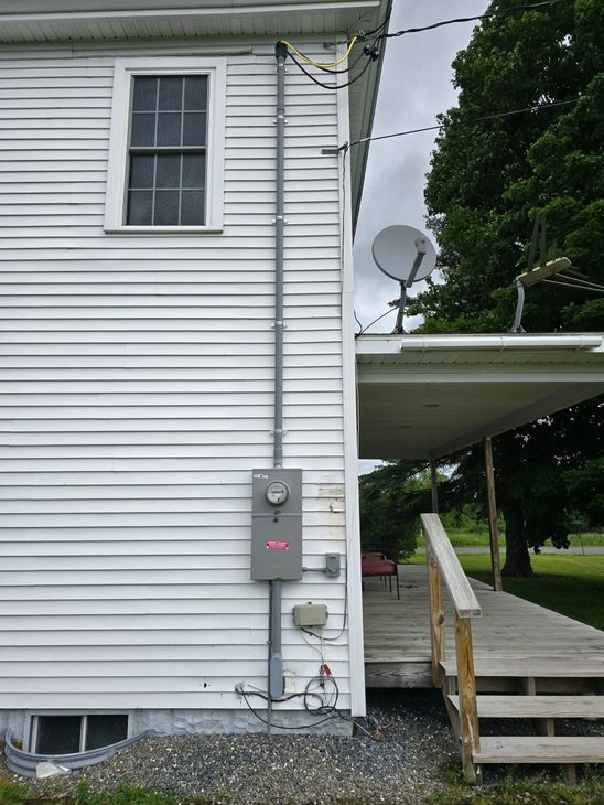 Gray house siding with electrical meter and utility boxes mounted on the exterior wall