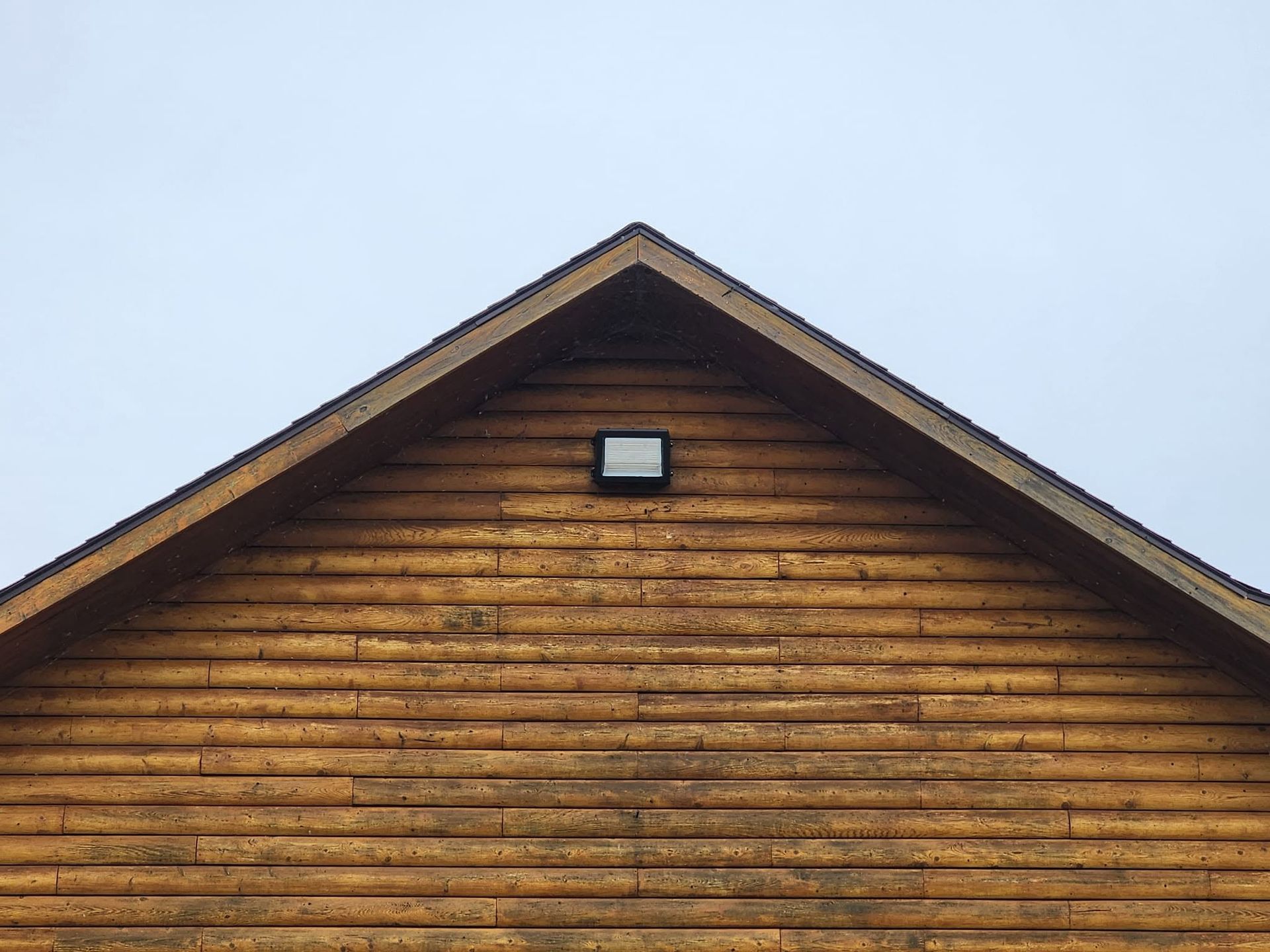 Wooden house gable with brown siding and a small square window against a blue sky