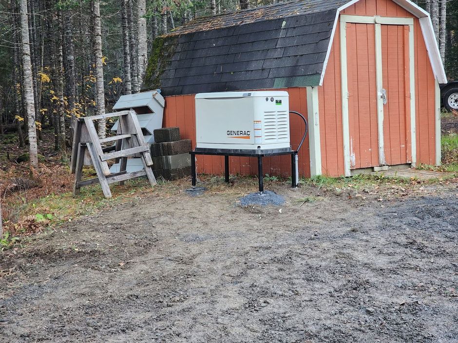 Small orange shed with white trim and generator beside a wooded dirt clearing