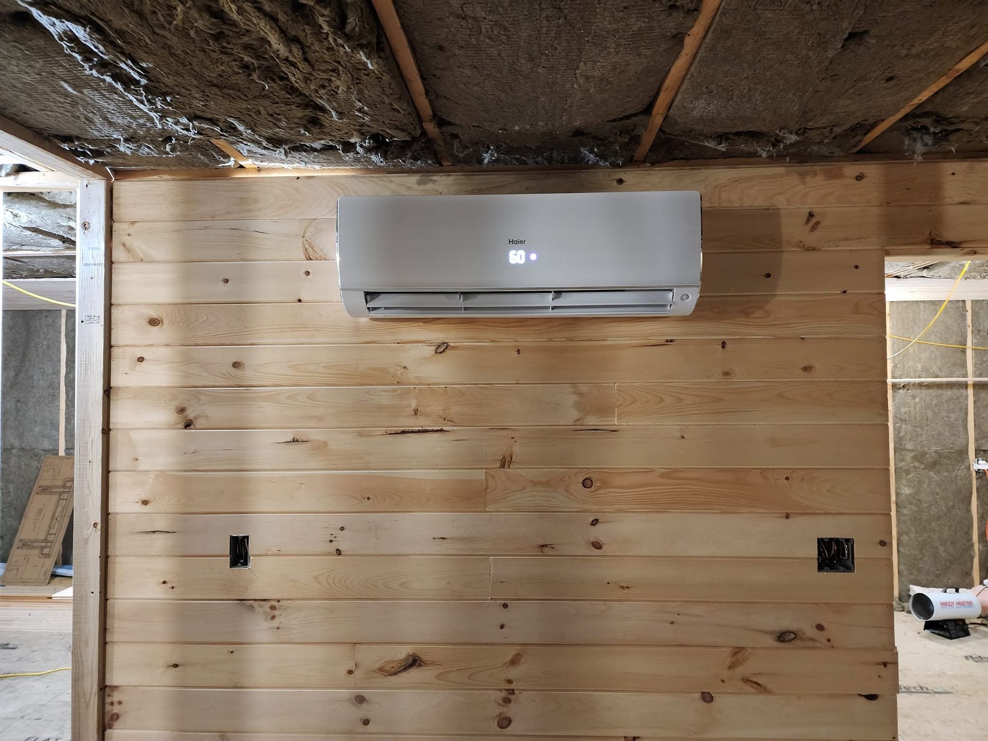 Partially finished room with a mounted mini split air conditioner on a wood-paneled wall