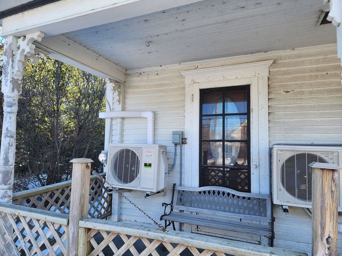 Front porch with white siding, two air conditioners, and a wooden bench by a glass door