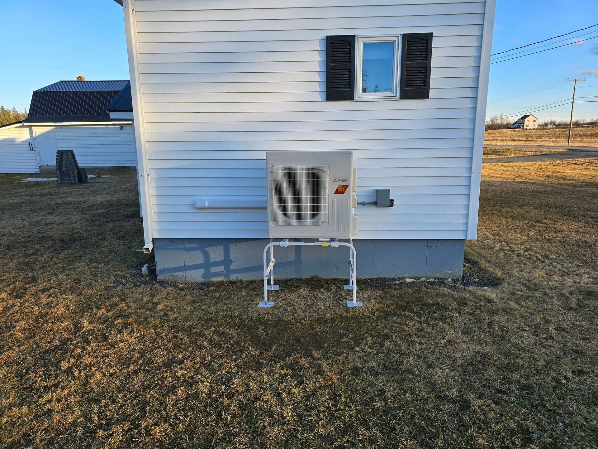 Small white house exterior with a wall-mounted mini-split AC unit and two windows above it.