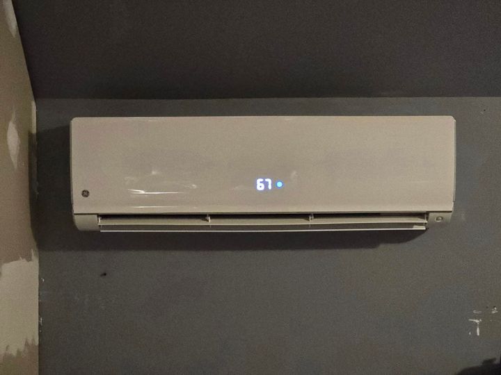 Wall-mounted white air conditioner on a gray wall, displaying 63°