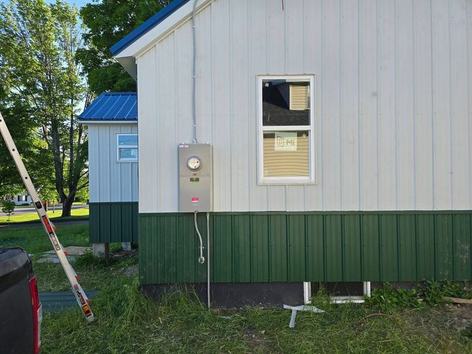 White house exterior with green lower siding and an electrical meter box mounted on the wall