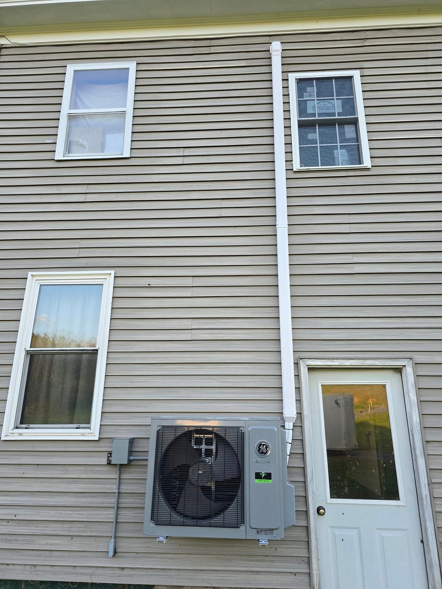 House exterior with beige siding, two windows, a white door, and an air conditioner unit.