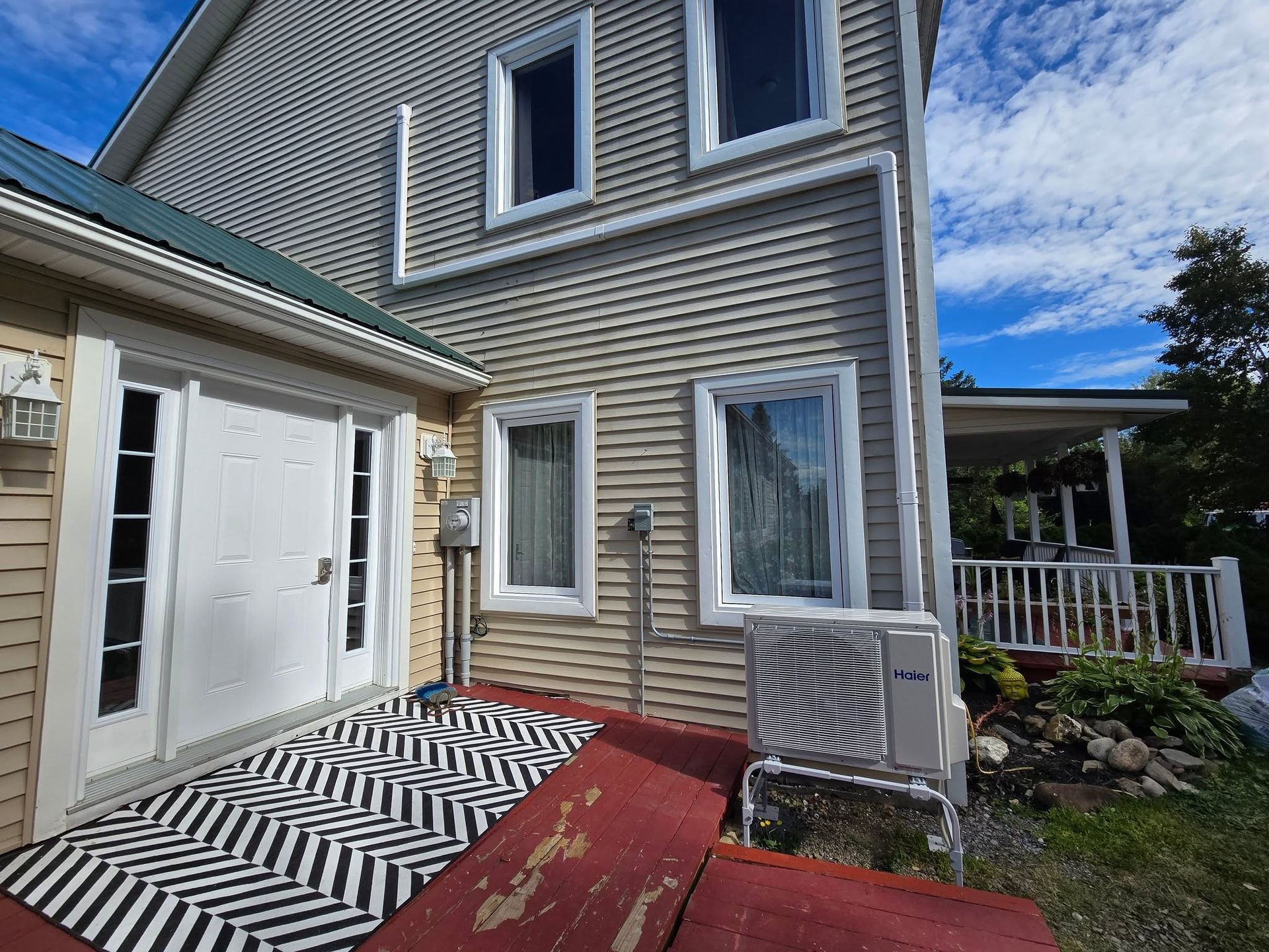 House exterior with white siding, red deck, and black-and-white striped rug beside a porch.