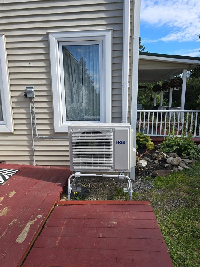 House exterior with a window-mounted air conditioner beside a red wooden deck and porch.