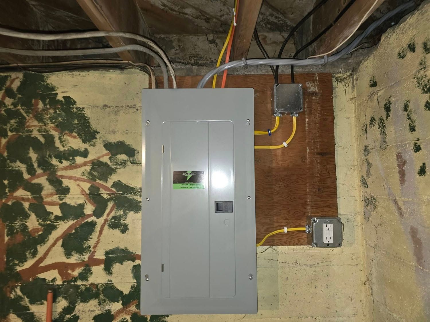 Electrical breaker panel mounted on a basement wall with exposed yellow wiring and pipes nearby