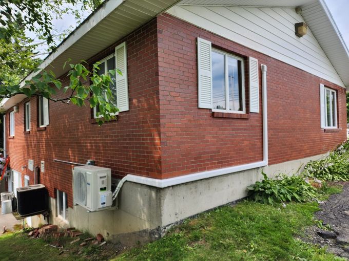 Red brick house exterior with white trim, small windows, and visible utility units beside the foundation