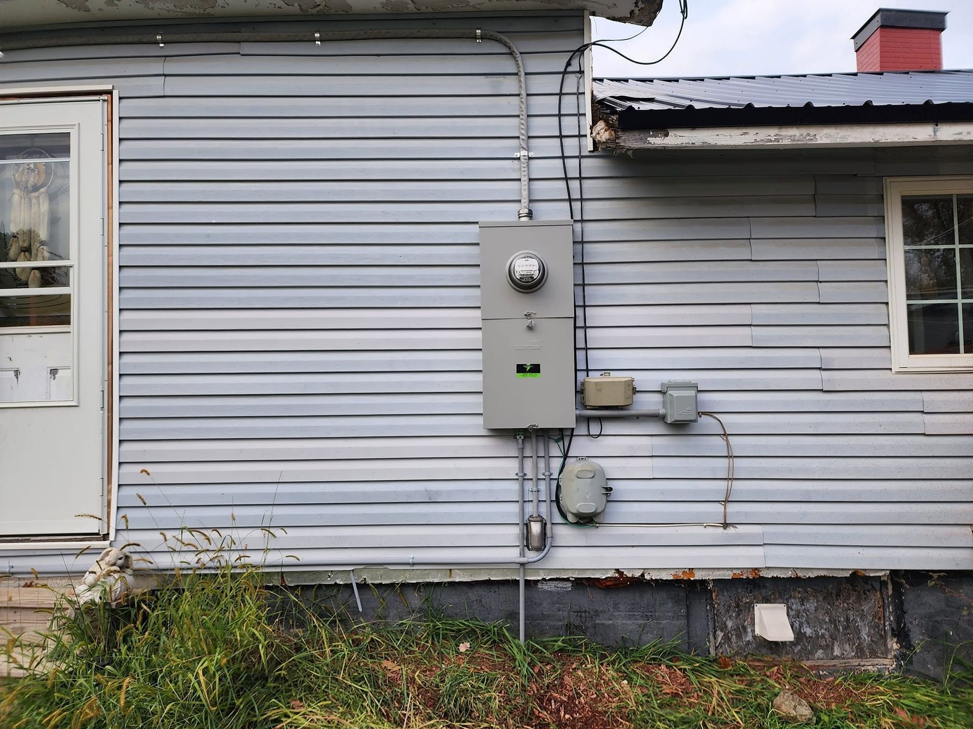 Gray house siding with electrical meter and utility boxes mounted on the exterior wall