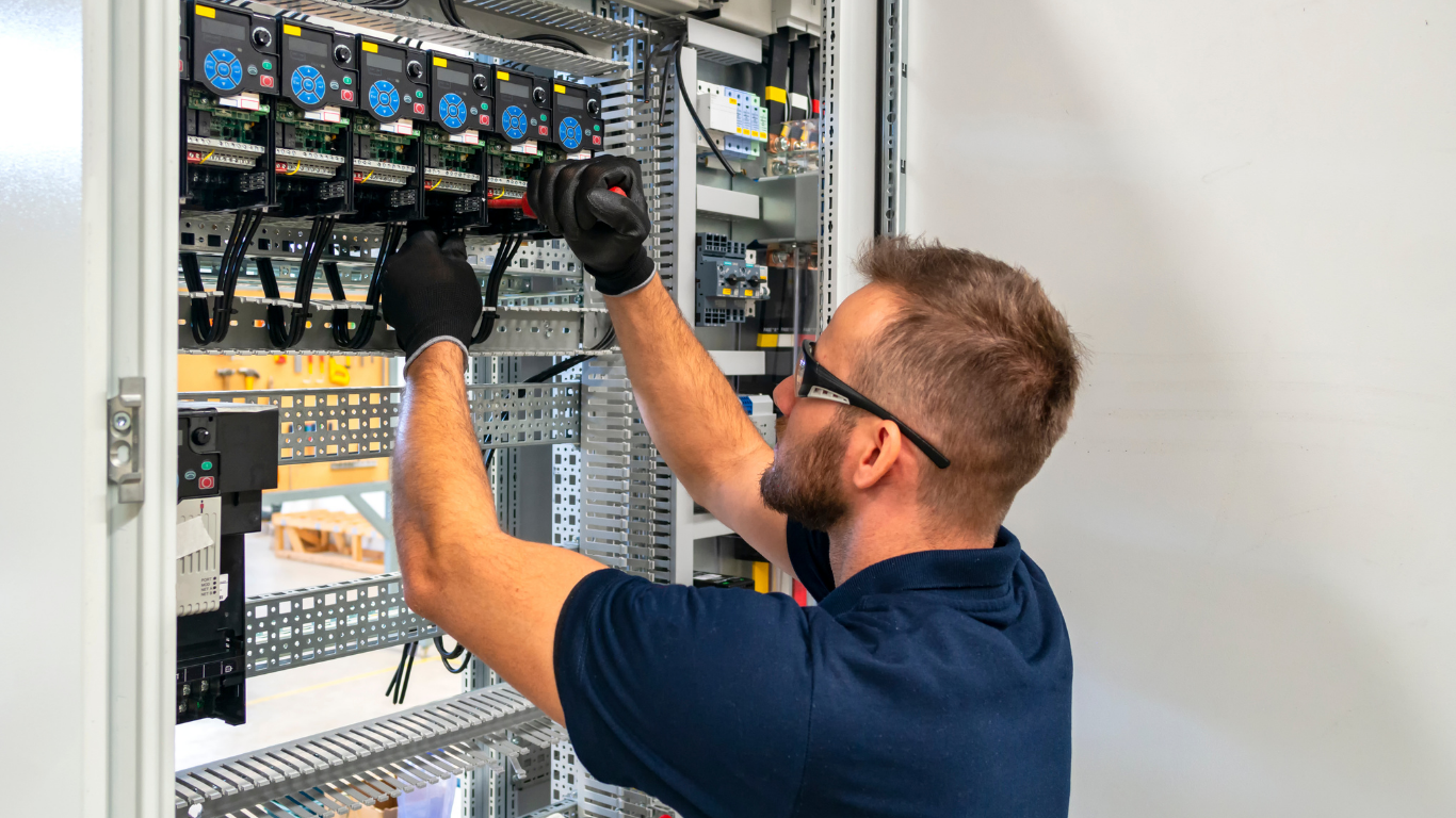 Technician working inside an open electrical control panel, adjusting wiring with gloved hands.