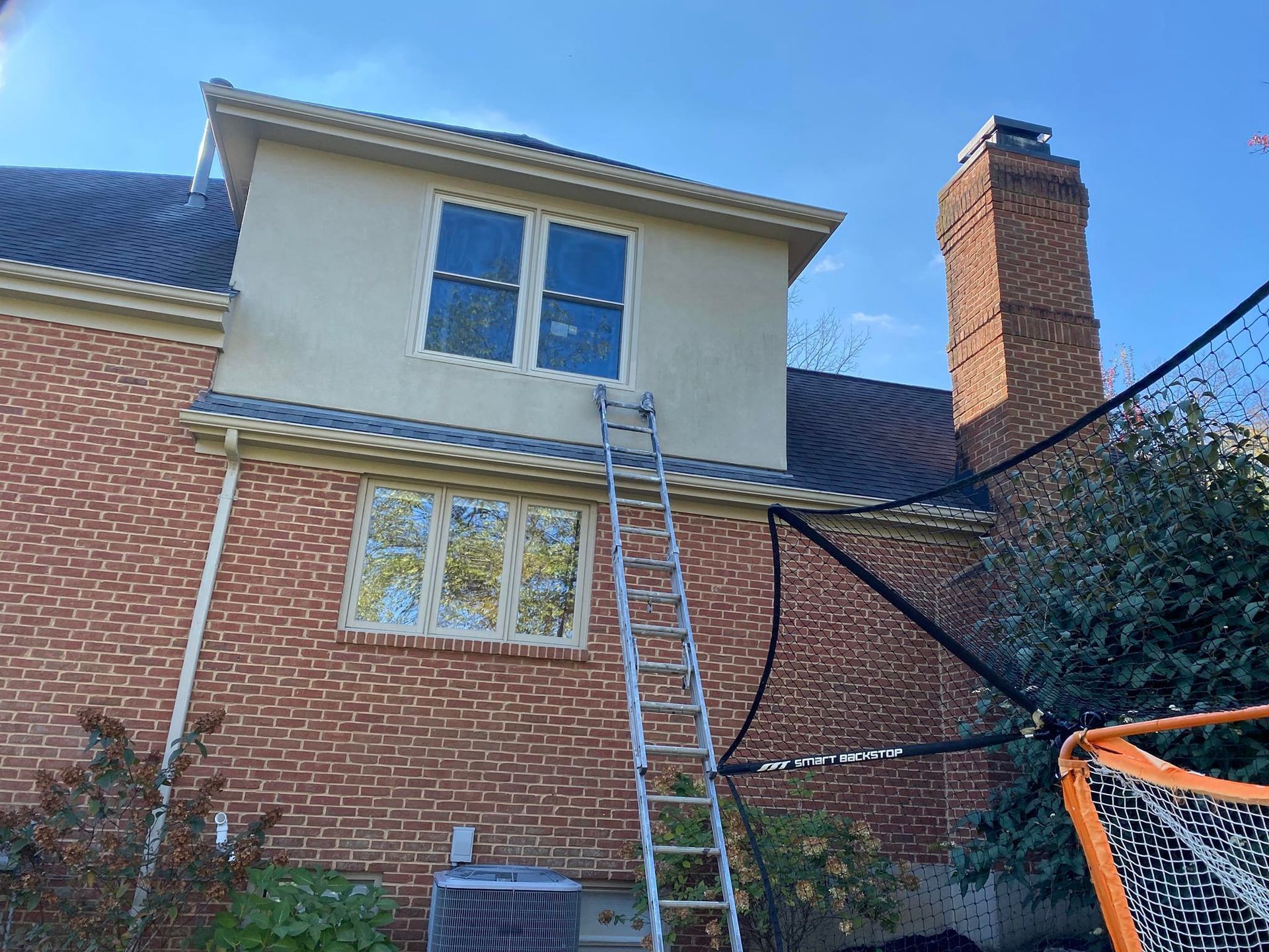 Brick house with ladder to upper windows, stucco wall, and chimney.