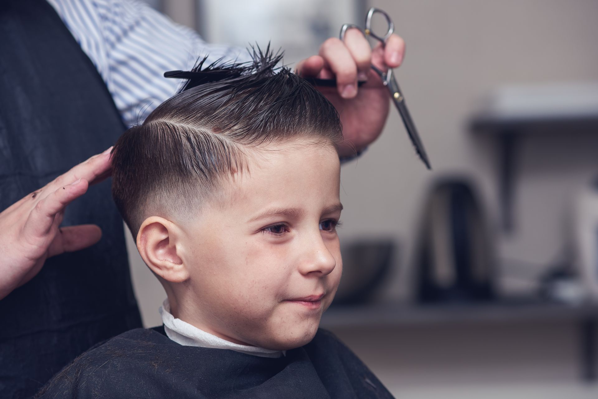 Ein kleiner Junge lässt sich von einem Friseur die Haare schneiden.