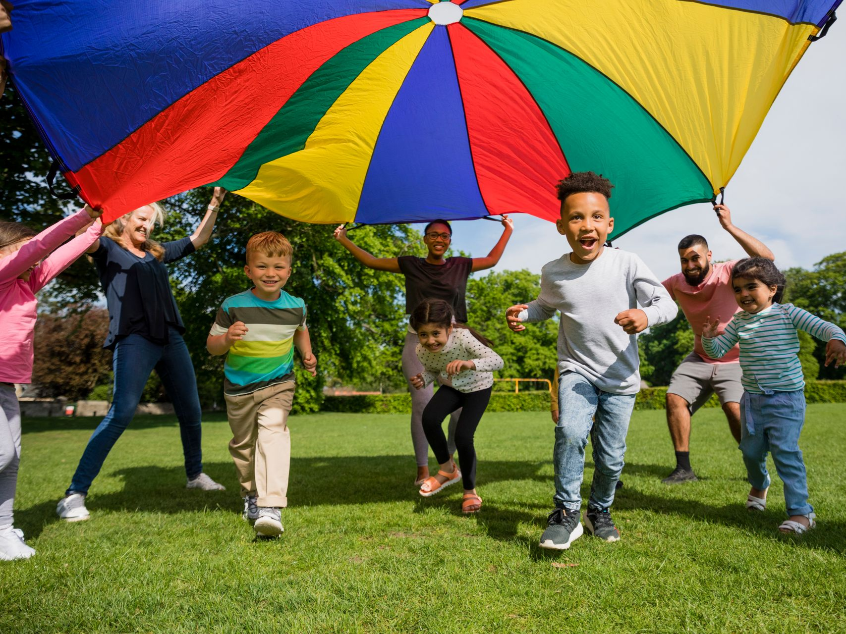 People running under a colorful parachute on a grassy park lawn