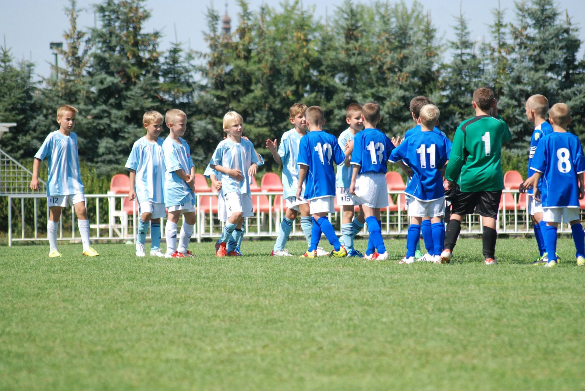 Youth soccer teams lined up on a grassy field, with players in light blue and dark blue uniforms.