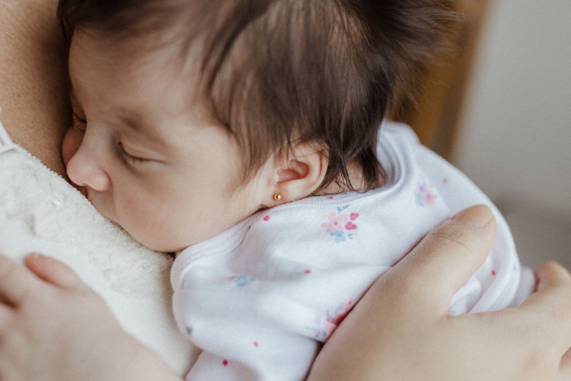 Sleeping baby resting against an adult’s shoulder, wrapped in a white patterned blanket