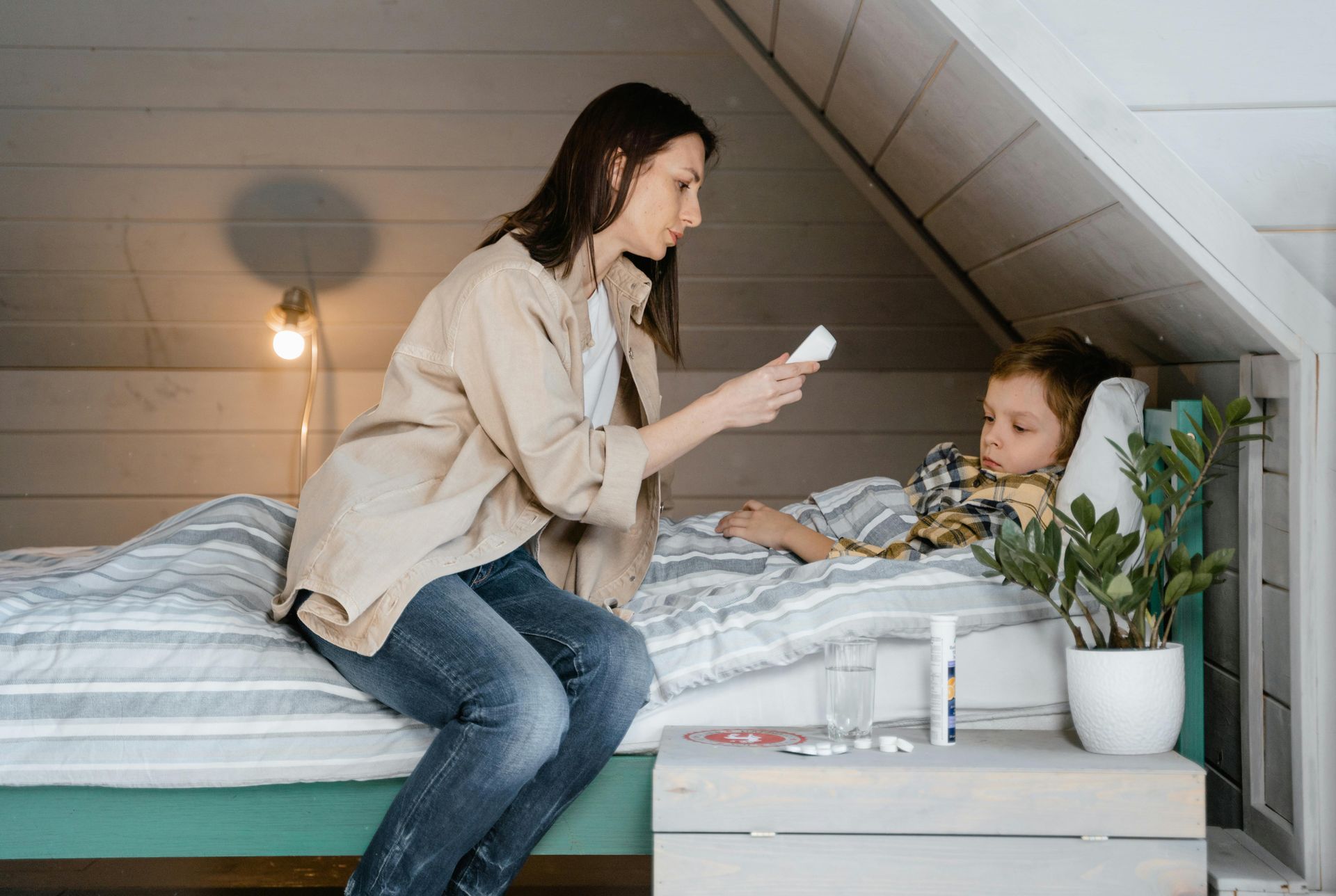 Woman sitting on a bed offers medicine to a child in a cozy bedroom under the attic roof