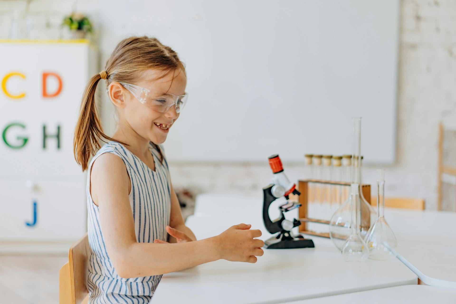 Young girl wearing safety goggles doing a science experiment with lab glassware in a classroom