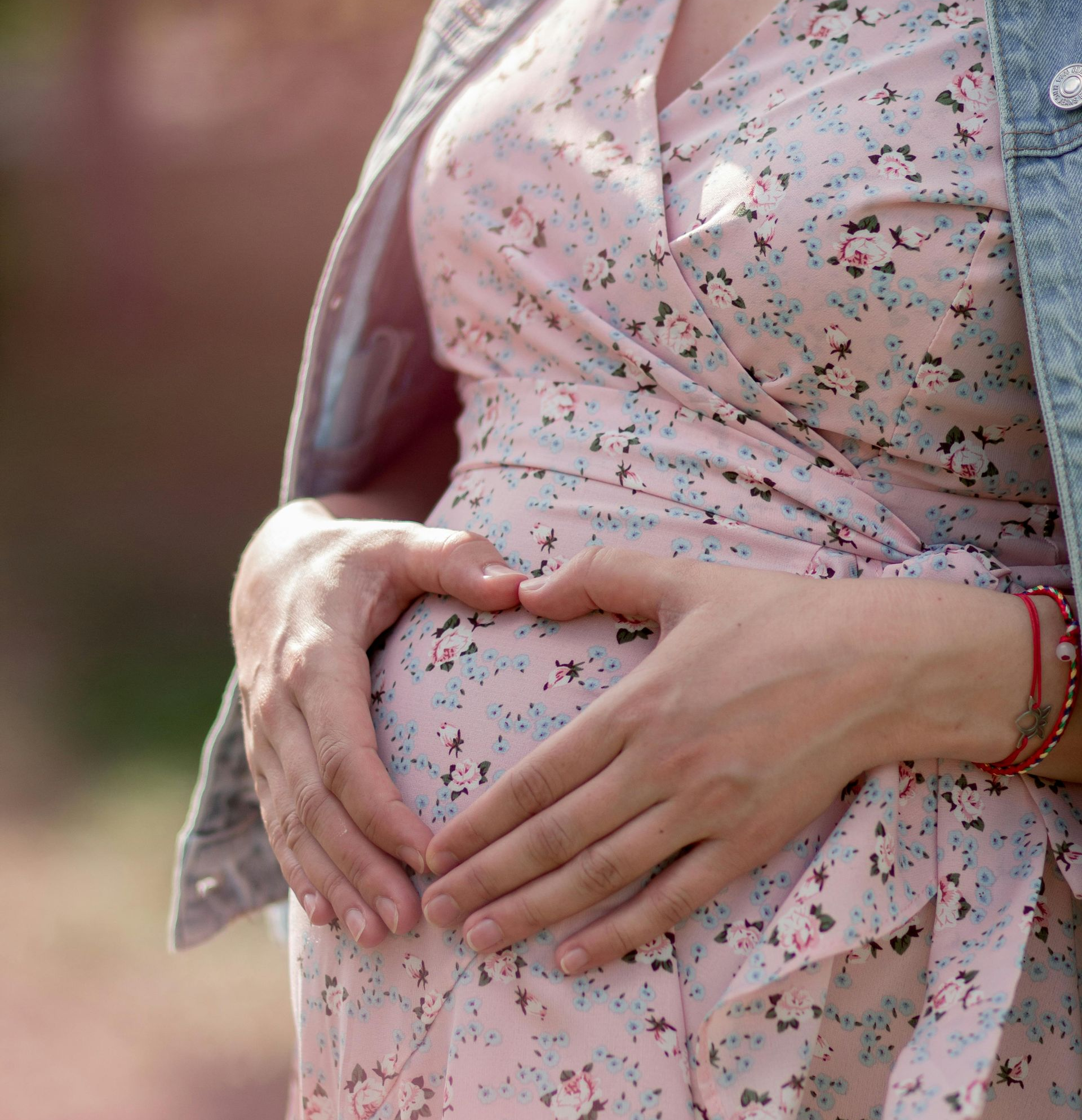 Hands forming a heart over a pregnant belly in a pink floral dress