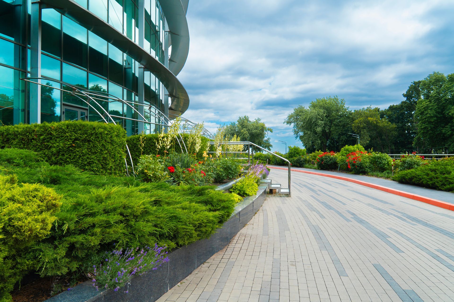 A landscaper installing fresh green sod next to a landscaped area with decorative stones and plants Business center building with glass facade and landscaping featuring green bushes and flowers.