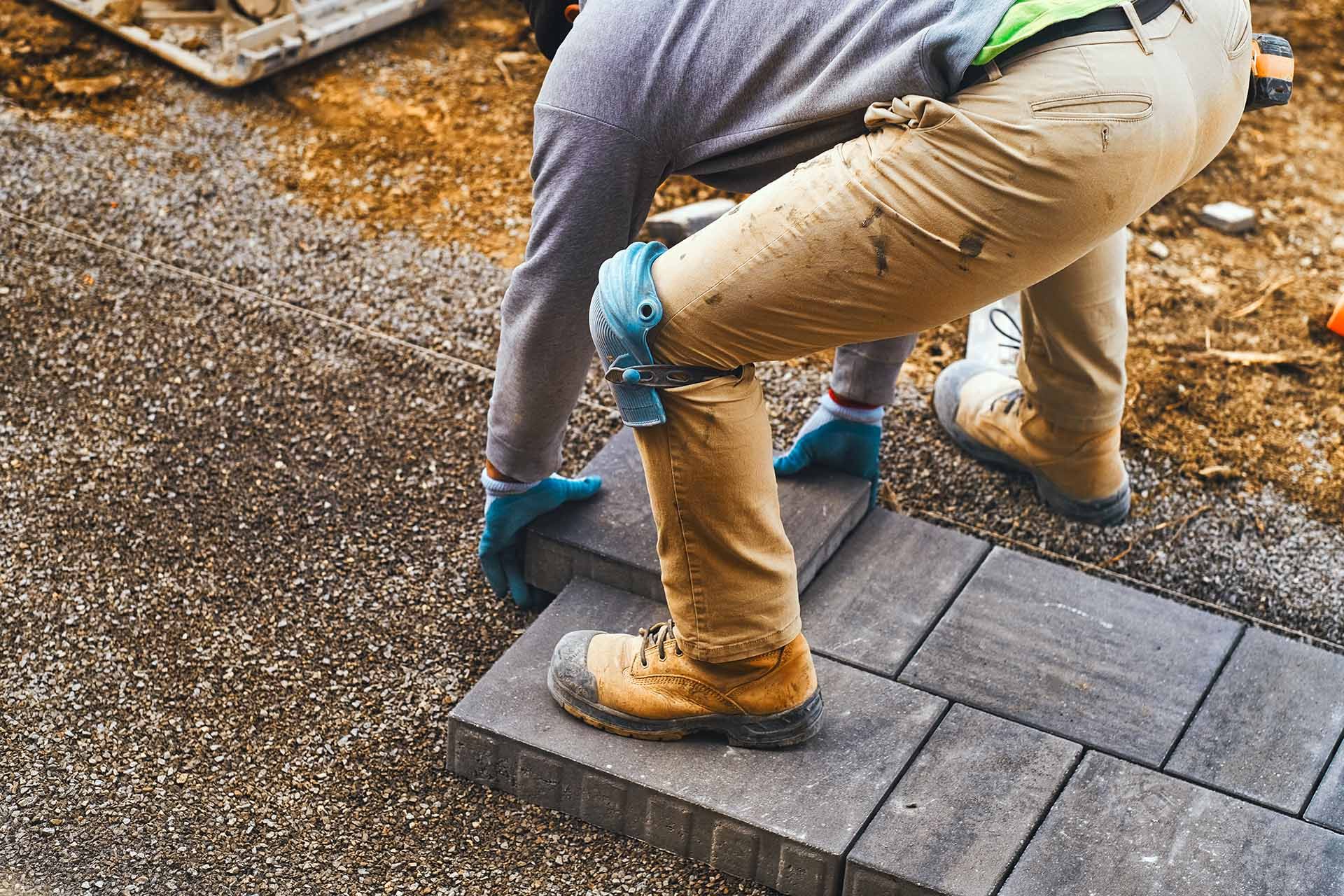 A man working diligently on a brick walkway, enhancing the outdoor space for a landscaping company. A man working diligently on a brick walkway, enhancing the outdoor space for a landscaping company.