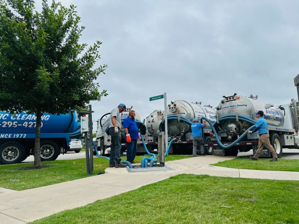 Workers beside cement mixer trucks on a sidewalk near a grassy street under cloudy skies