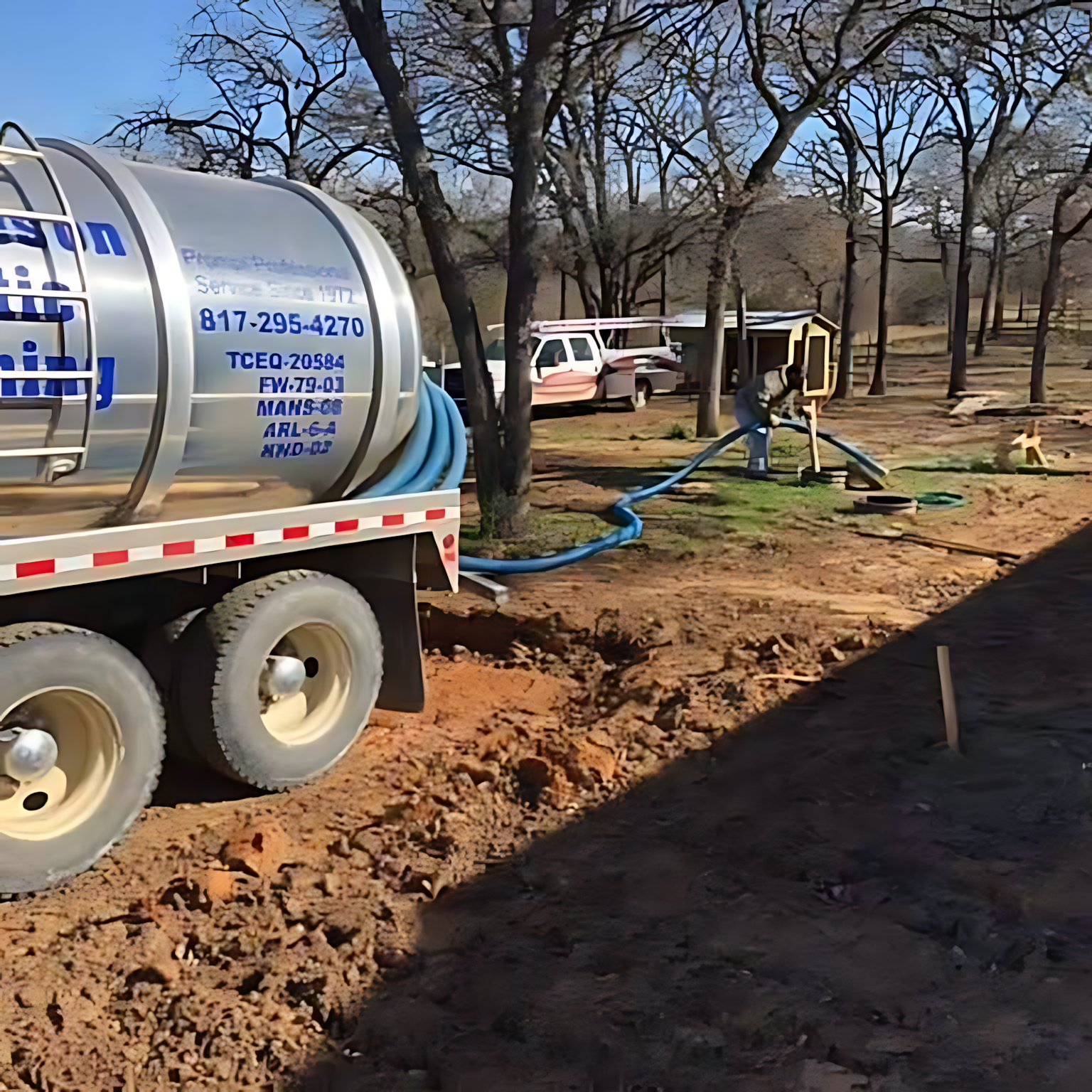 Water tanker truck pumping blue hoses into a trench at a rural work site
