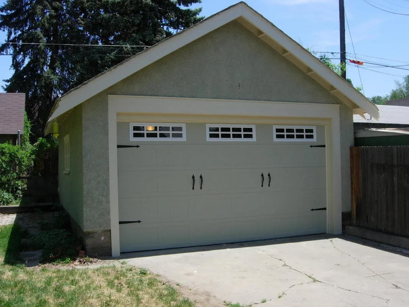 Light green detached garage with a tan door and white trim.