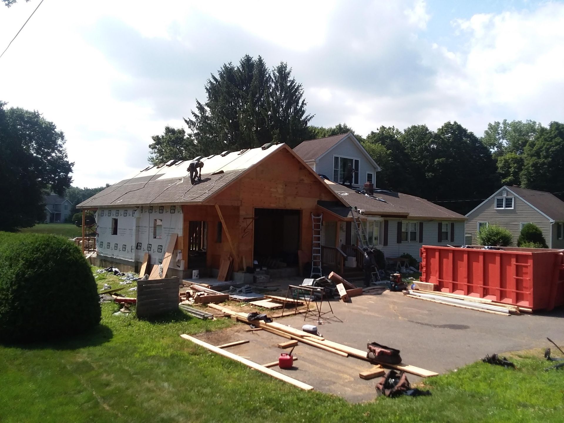 House undergoing construction with exposed framing and a dumpster in the driveway.