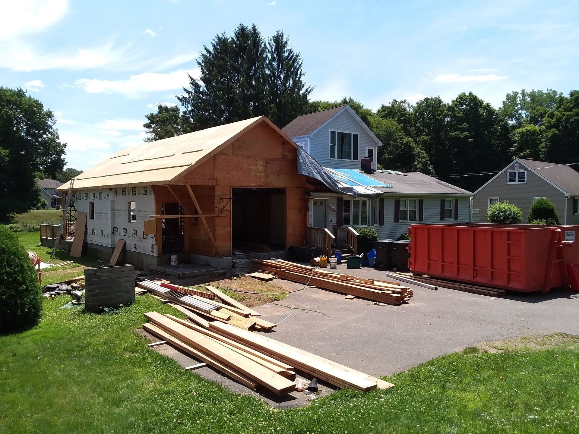 Garage under construction next to a house with an orange dumpster on the driveway.