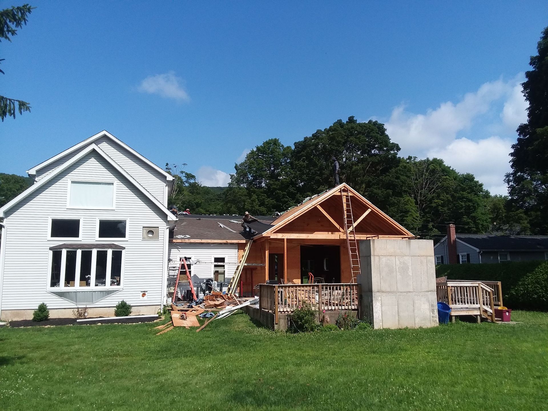 Construction site with white house, wooden frame structure, blue sky, and green lawn.