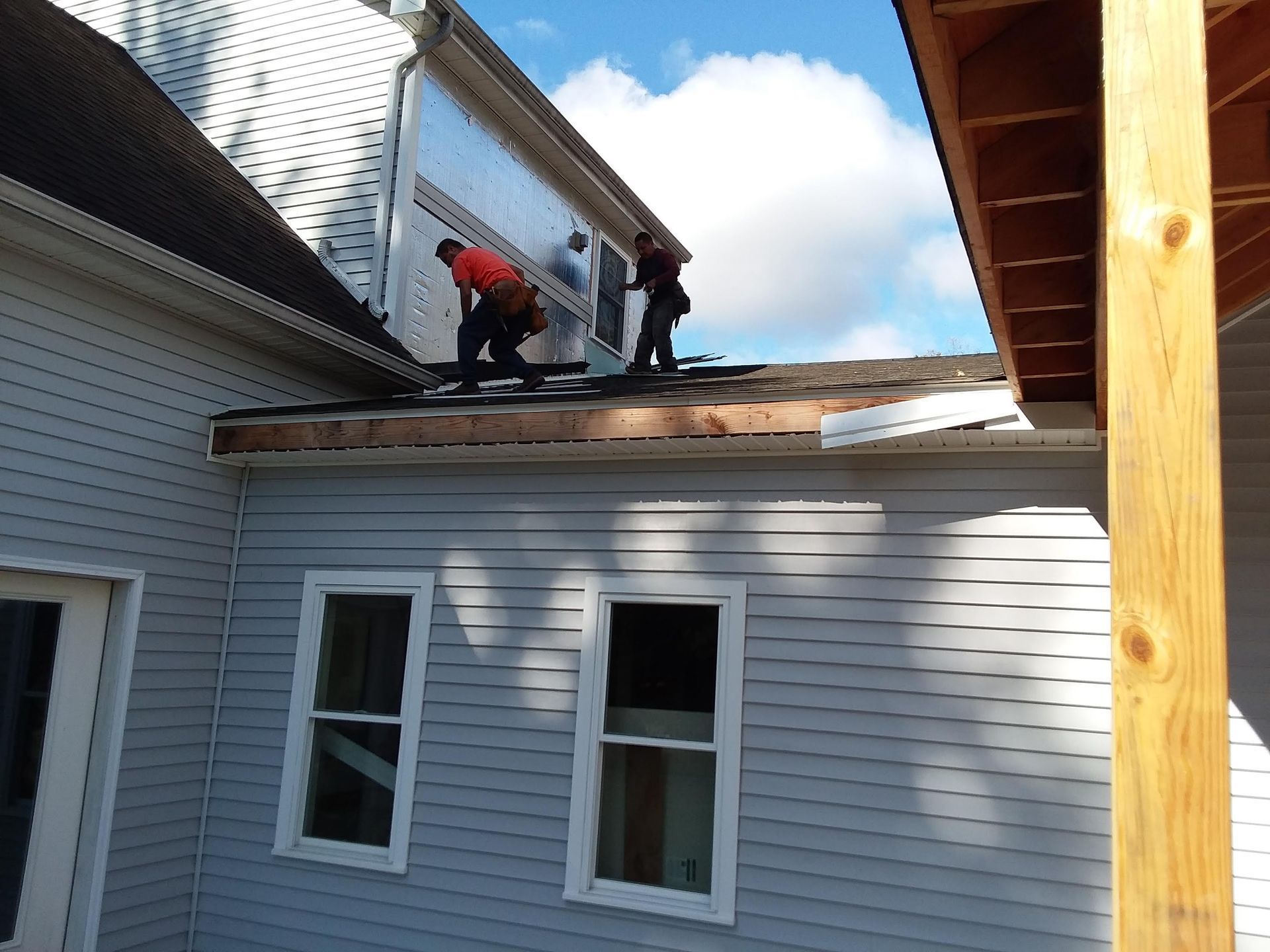 Roofers working on a house, sky, siding, wood beams, and a glimpse of an adjacent porch.