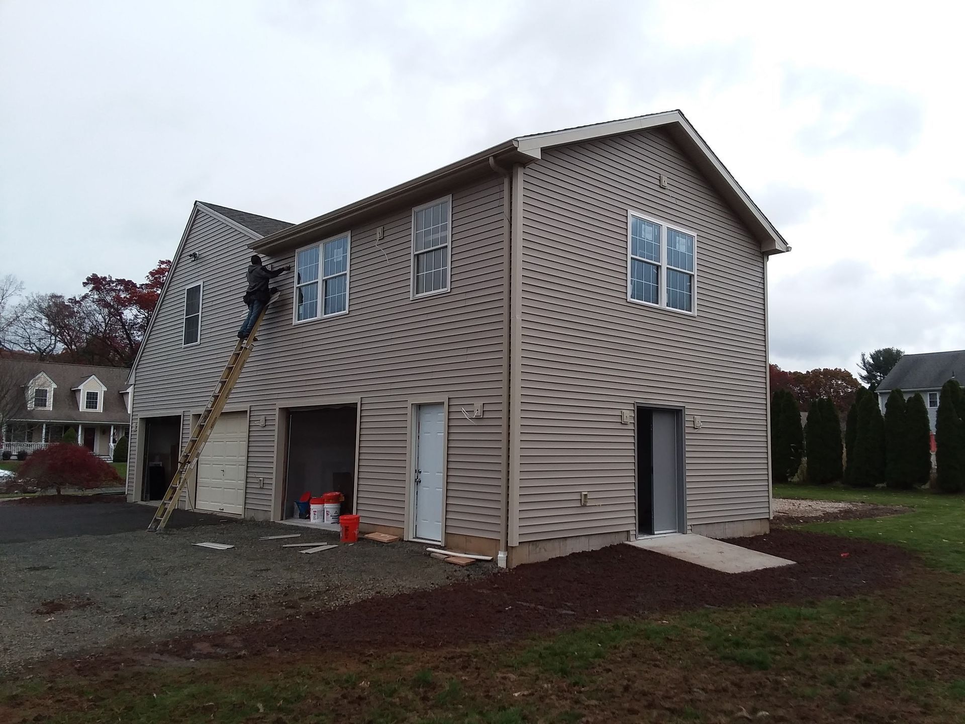 Two-story building under construction with tan siding, several windows, and a ladder against the side.