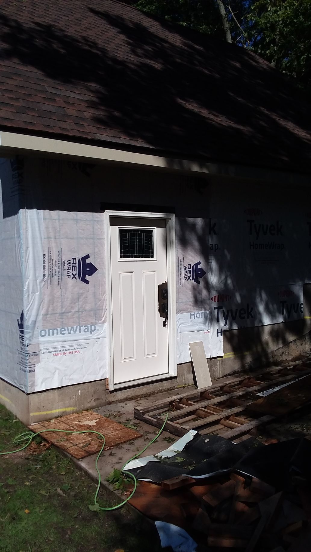 Exterior view of a building with a white door, brown roof, and blue protective wrap.