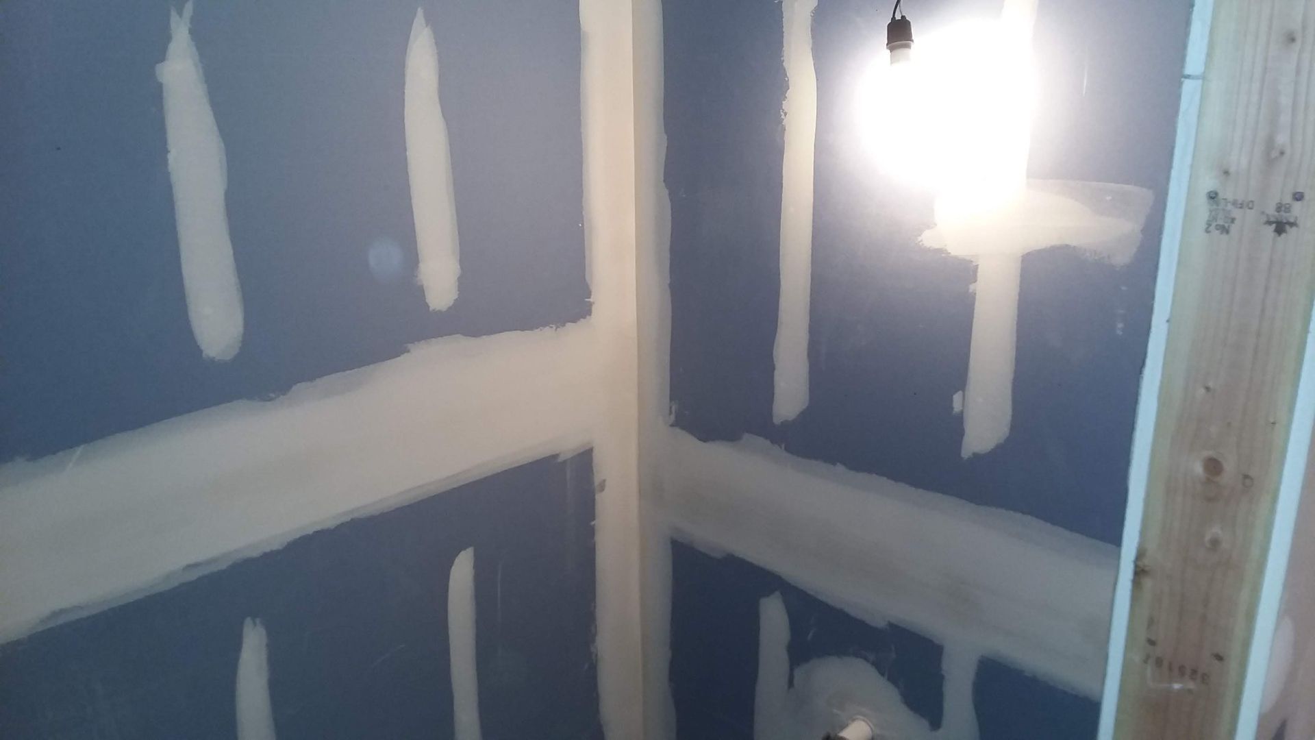 Blue drywall with white joint compound in a room under construction, with a bright light.
