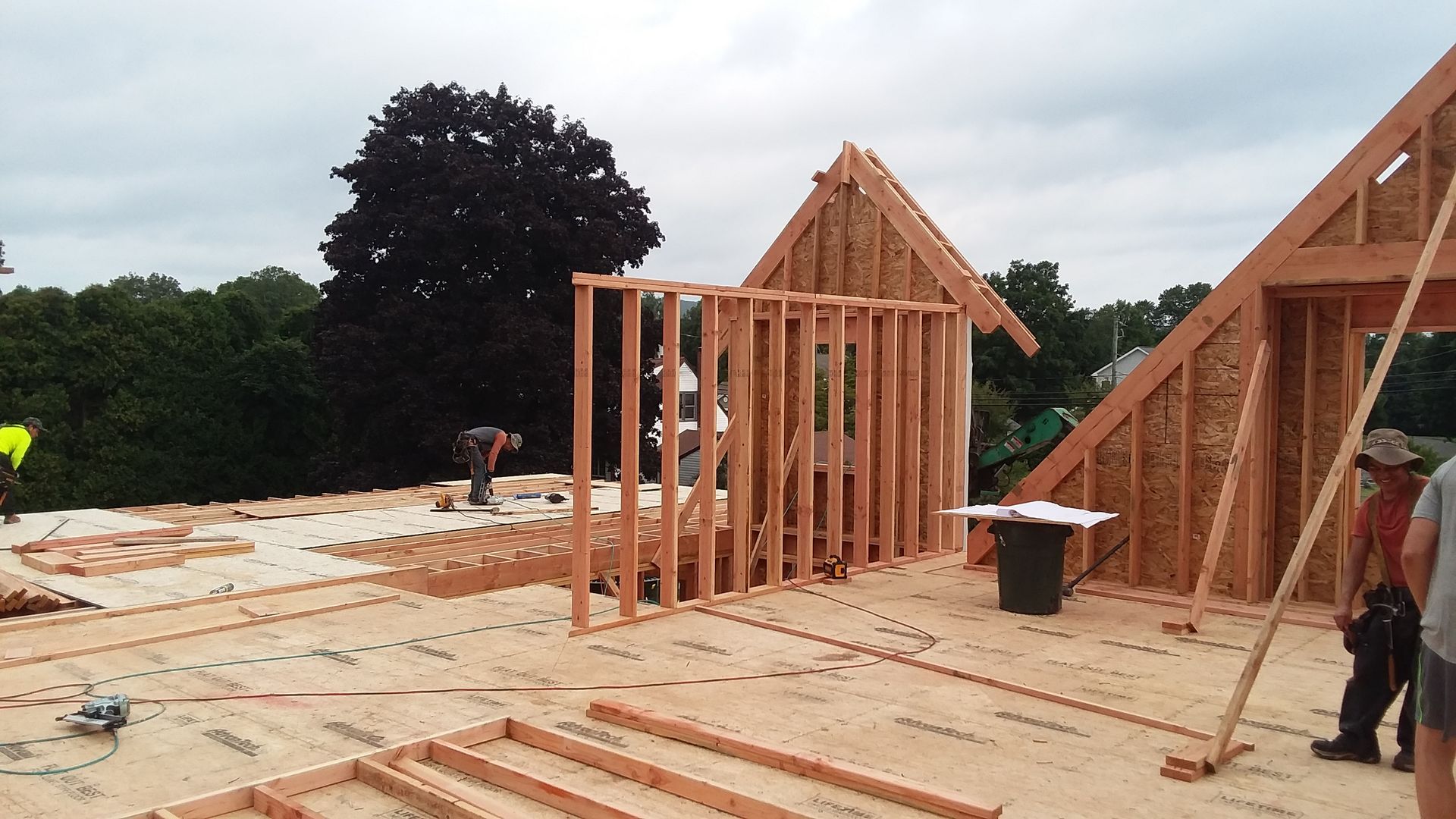 Construction of a wooden roof frame and interior wall on a flat surface, outdoors. Workers build a structure.