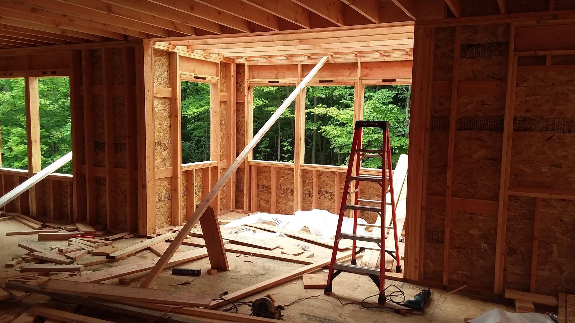 Interior framing of a house under construction; windows and ladder are visible.