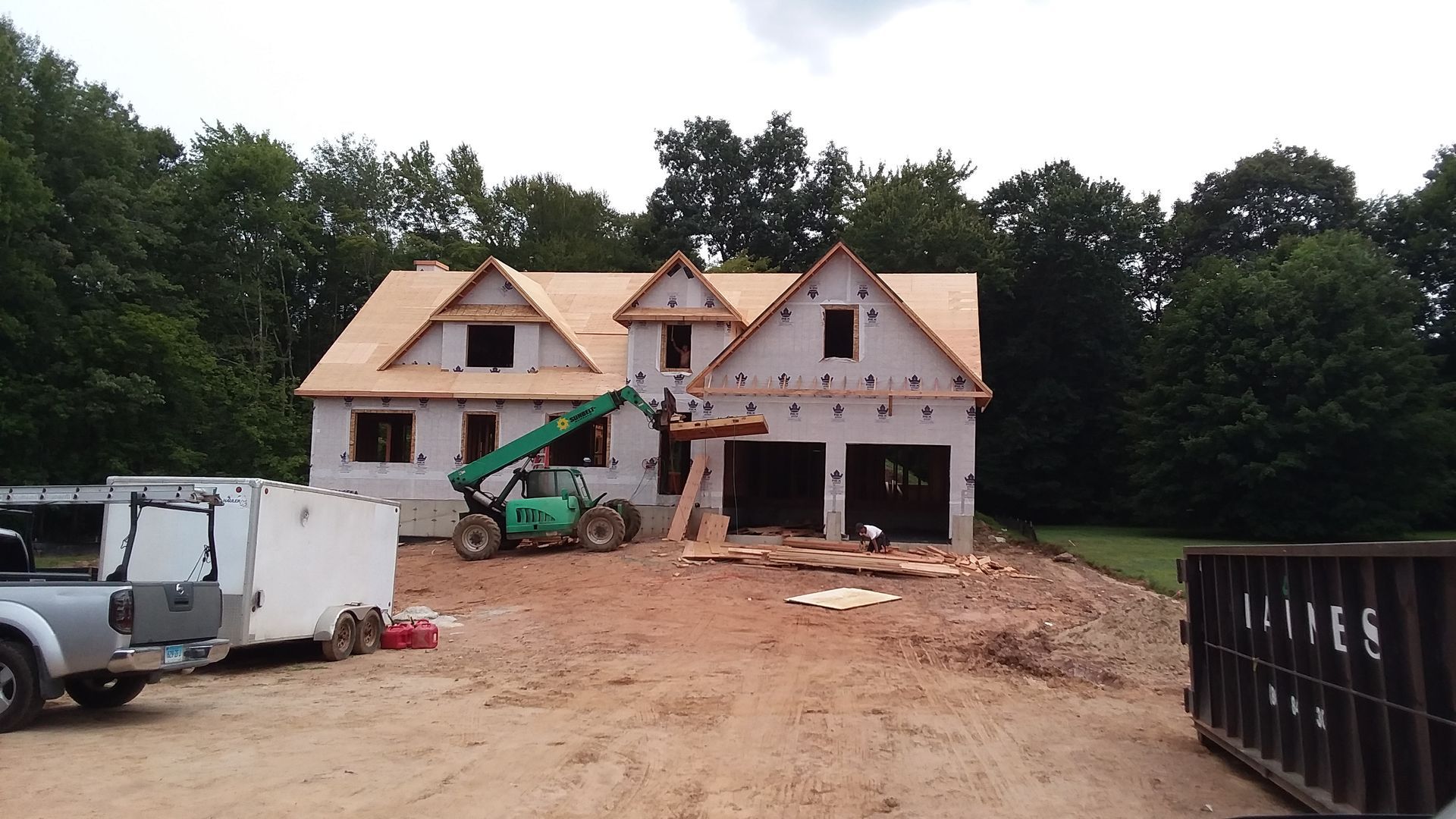 House under construction with a lift. Brown roof, white walls, and a construction site.