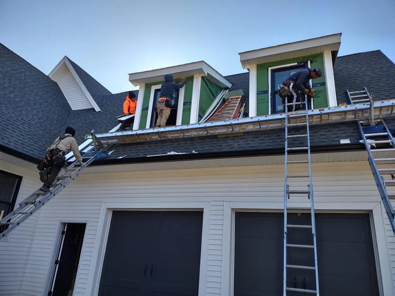 Construction workers on a roof, installing siding and working on dormers, sunny day.