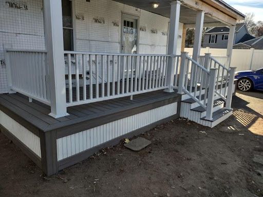 Newly constructed porch with gray composite decking, white railing, and paneled skirting.