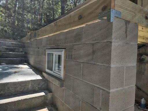 Cinder block wall with a small window, stairs to the left, and wooden beams overhead.
