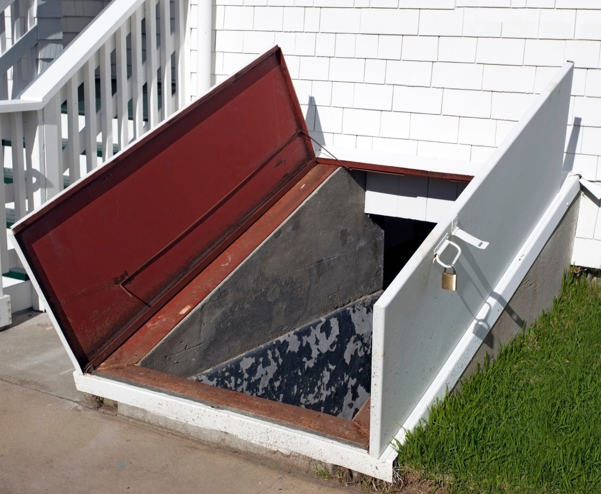 Open basement door with red and white panels; locked. Located next to white house and stairs.