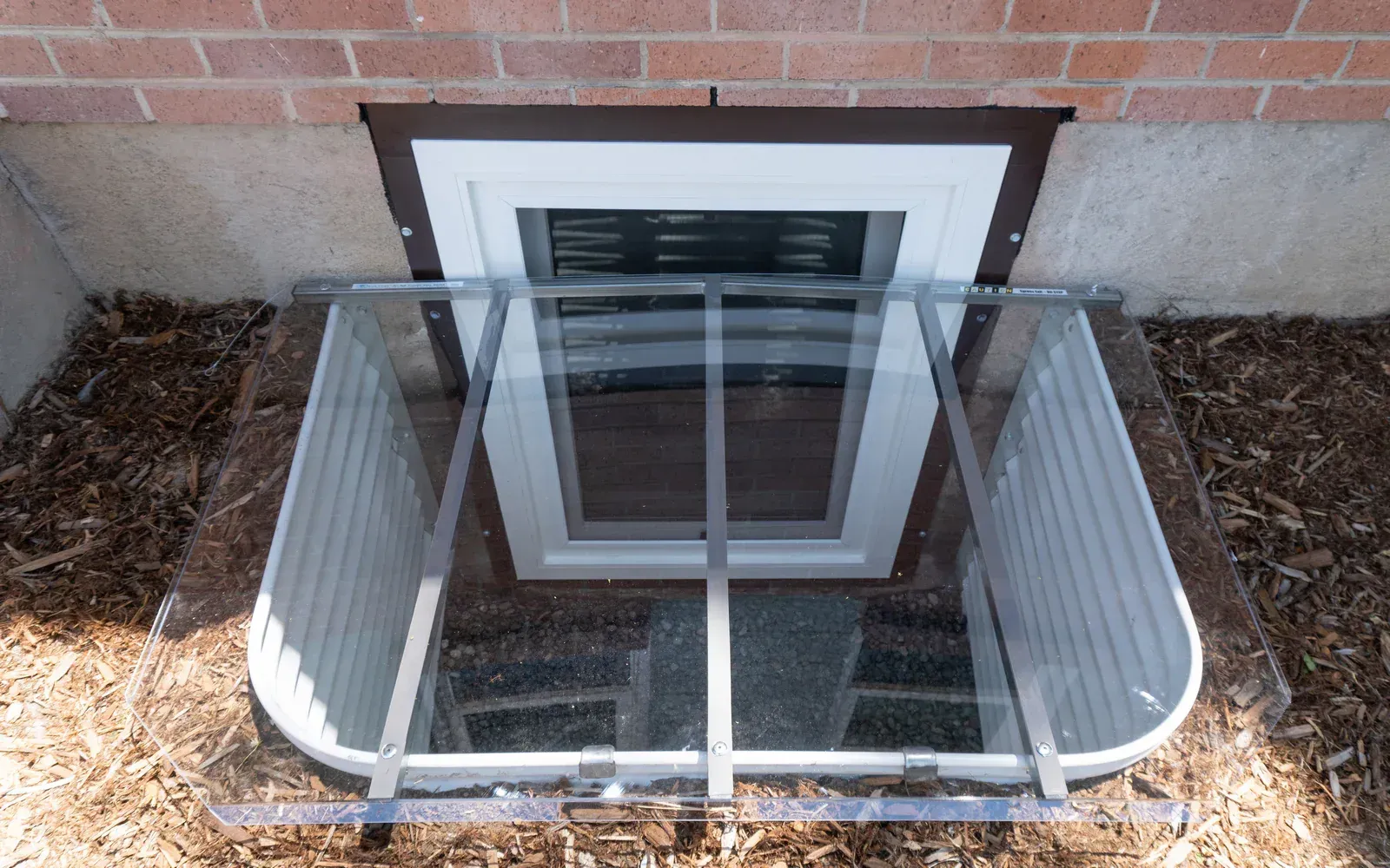 Window well with clear cover and security bars, set into a brick wall.