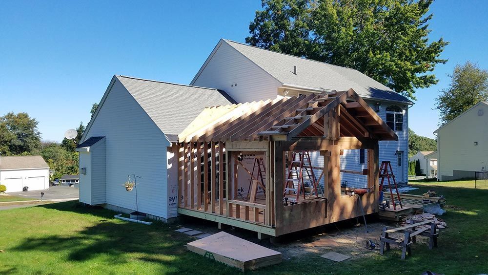 House with new wooden porch under construction; blue sky and green grass.
