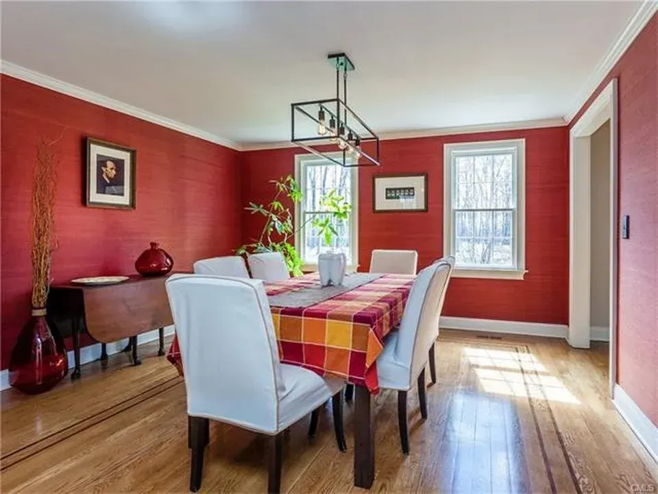 Dining room with red walls, wood floor, table with chairs, and natural light from windows.