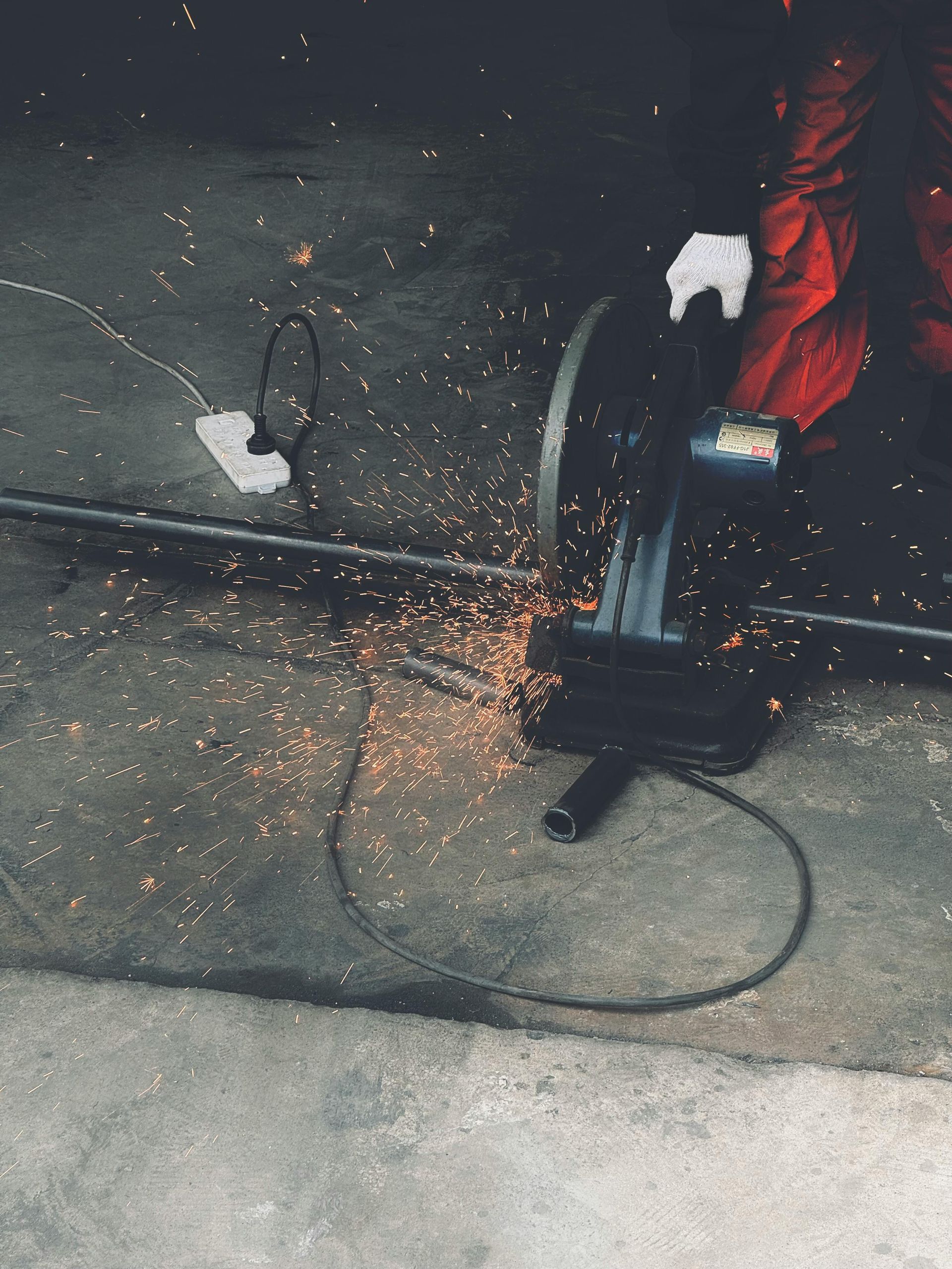 Person in red coveralls uses a chop saw, creating sparks as they cut metal.