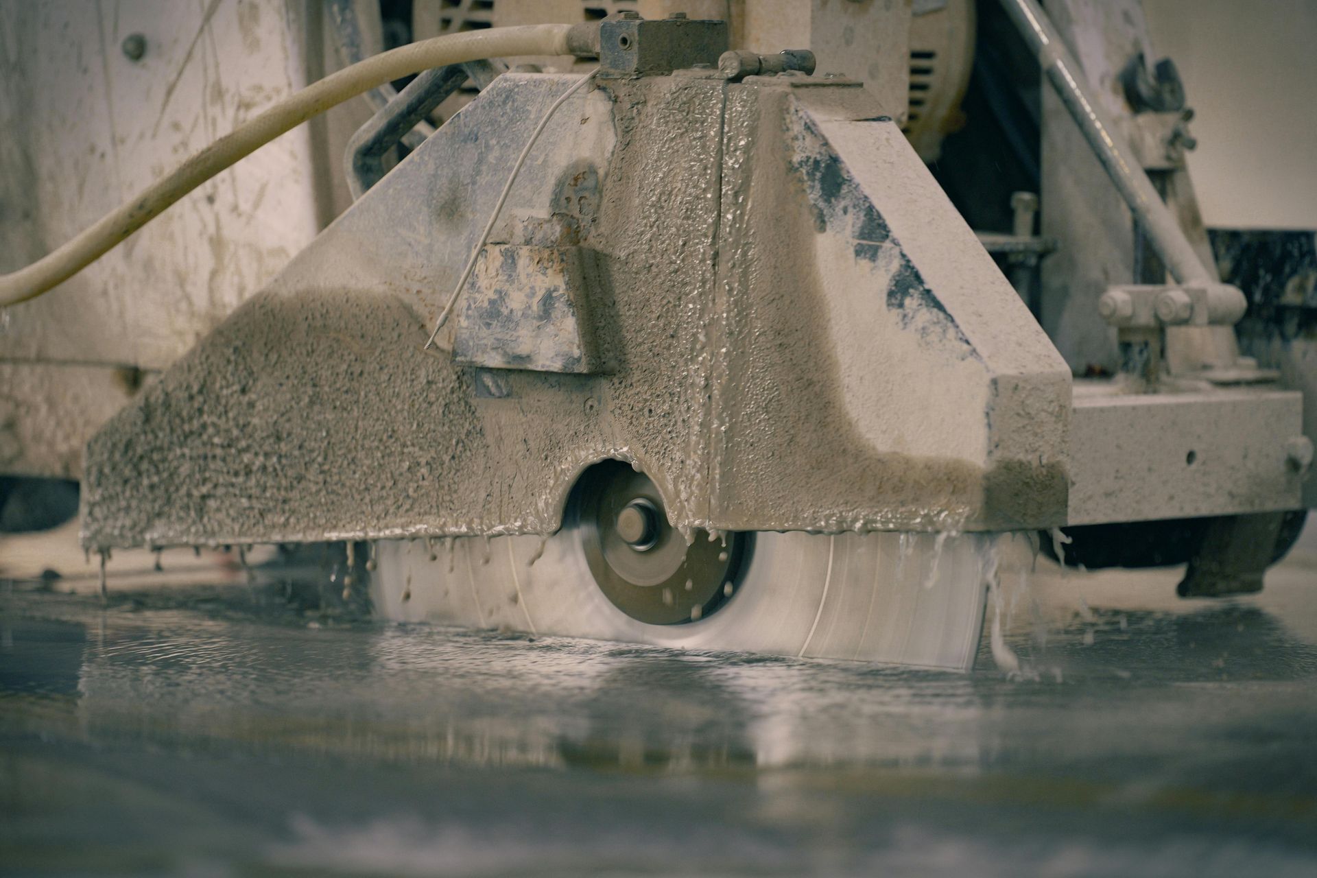 A concrete saw cutting through a wet, light gray surface, creating a trail of debris and water.